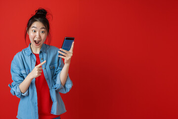 Naklejka premium Excited Young Woman in Red and Blue Outfit Holding Smartphone and Pointing Upwards - Generative AI