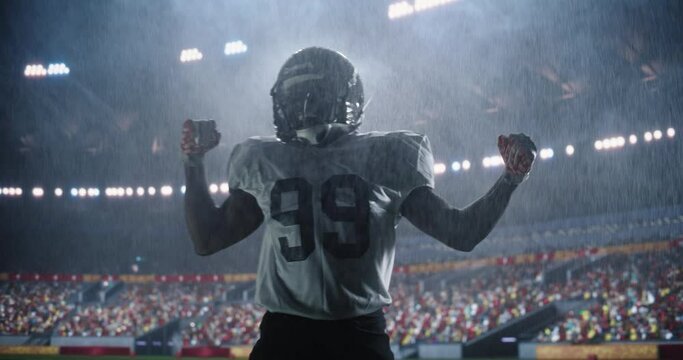 Portrait of Male Football Player Celebrating Scoring a Successful Touchdown Under Heavy Rain. Athletic American Footballer Jumping on a Stadium Field. Crowd Cheering In The Background