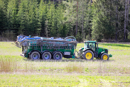 John Deere 7230R tractor and Samson PG slurry tanker in stubble field to inject liquid manure for fertilization. 