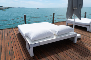 Sunbeds on wooden pier on shore of sea in summer landscape. Sunchairs on wooden deck by the ocean....