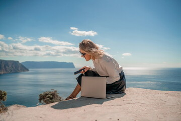 Freelance women sea working on a computer. Pretty middle aged woman with computer and phone outdoors with beautiful sea view. The concept of remote work.