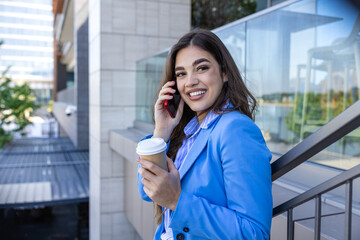 Beautiful young woman talking on her mobile phone and smiling at the staircase drinking coffee....