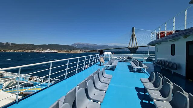 Young woman walking on windy ferry deck with Rio bridge in background, Greece