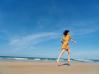 Woman running on sandy beach in yellow dress with ocean in background under clear blue sky