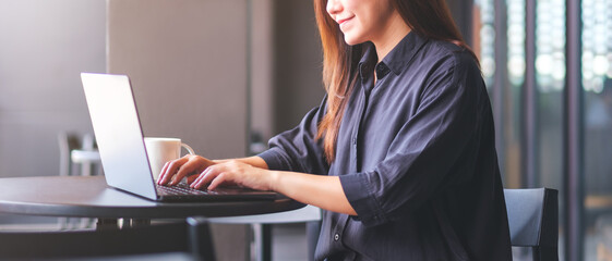 Closeup image of a young woman working and typing on laptop computer in cafe