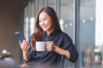 Portrait image of a young woman holding and using mobile phone while drinking coffee in cafe