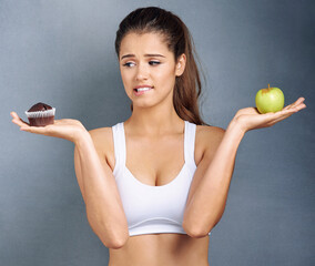 Woman, food and thinking of choice in studio with apple, muffin and confused with diet decision for...