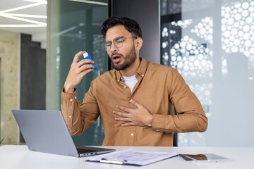 Asthmatic man using inhaler for relief while working in modern office