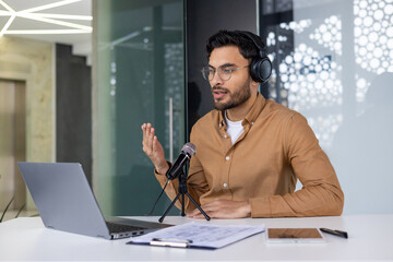 Young professional recording podcast using laptop and microphone in office setting