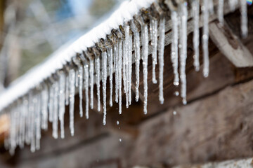 close up of many icicles on a roof of a cabin with water dripping down in winter
