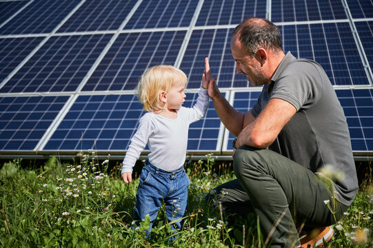 Young father and his little son giving each other high-five on background of solar panels. Young father glad spending time with his child. Happy family of two on background of solar panels.