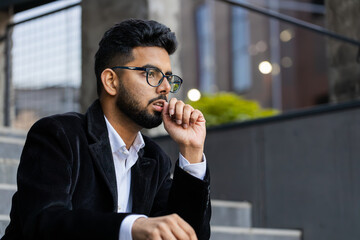 Unhappy sad Indian business man frustrated stress pensive feeling bad after company unemployment lost job problem solution crisis outdoor. Arabian Hindu freelancer guy sitting on stairs downtown city