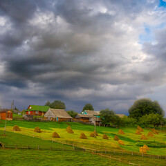 Obraz premium small village on green hill under dense cloudy sky