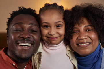 Close up portrait of happy African American family with little girl embracing and smiling at camera