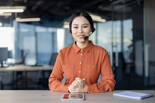 Smiling female customer service representative with a headset, working in a modern office environment with a tablet and notebook on the desk.