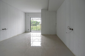 Fototapeta premium A bare white Primer color painted wall room with shiny marble tiled floor and lots of empty space. Unfinished room. Doors and electrical outlet have not yet been installed.