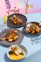 Stylish seafood ensemble featuring a grilled fish with caramelized onions and seared scallops on a creamy sauce, beautifully accompanied by a vibrant floral arrangement
