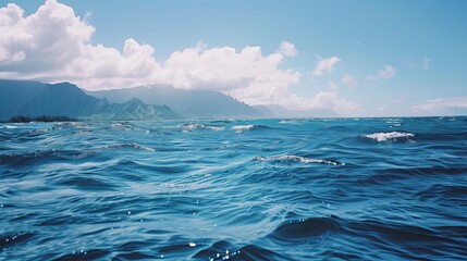 A blue ocean with a few waves and mountains in the background