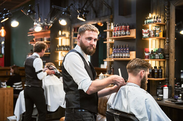 Handsome barber in elegant outfit shaving man's nape. Professional hairdresser using electric razor...