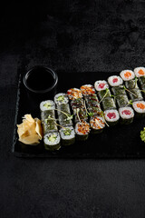 Assorted hosomaki sushi set with salmon, tuna, eel, and cucumber on black textured background