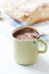 A cup of cocoa with yeast dough in the background. All on a light wooden background. Copy space.