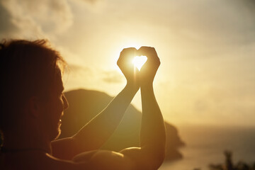Heart hands, sun and man at a beach with finger frame for sunset, freedom and adventure outdoor. Flare, sunrise and male with palm shape love at the sea for travel, journey and experience gratitude