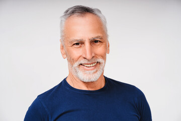 Smiling senior man with beard and gray hair looking at camera, isolated on white background