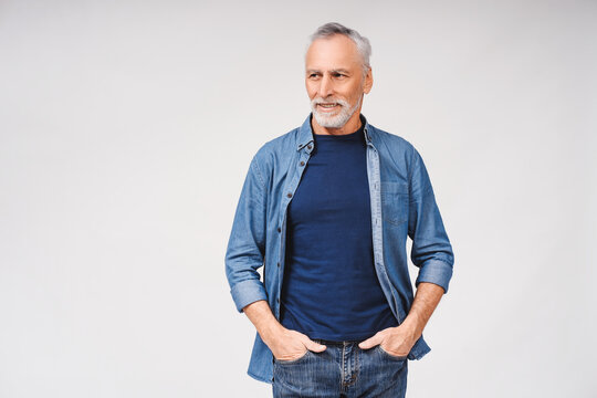 Smiling mature grey haired man holding hands in pockets against over white background