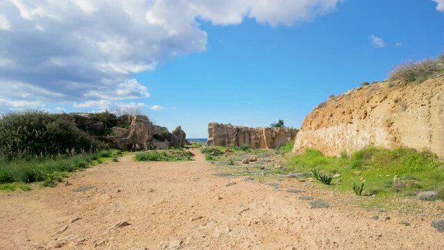 A pathway through rocky ruins at the Tombs of the Kings in Pafos, Cyprus, under a bright blue sky.