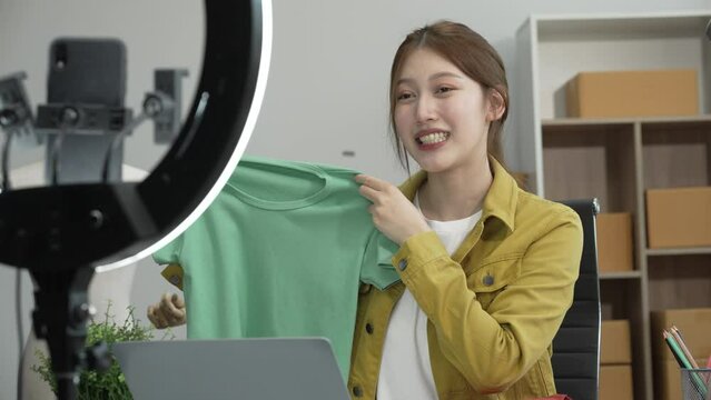 A young Asian businesswoman efficiently manages SMEs, utilizing her desk, tablet, laptop to handle online orders and live streams, showcasing entrepreneurial prowess in the dynamic market landscape.