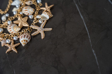Gold necklace in a nautical style against a background of black marble: starfish, pearls and shells