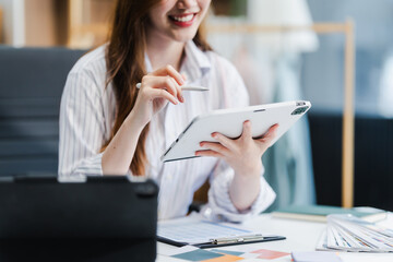 A young Asian businesswoman efficiently manages SMEs, utilizing her desk, tablet, laptop to handle...