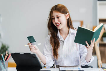 A young Asian businesswoman efficiently manages SMEs, utilizing her desk, tablet, laptop to handle...