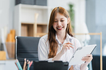 A young Asian businesswoman efficiently manages SMEs, utilizing her desk, tablet, laptop to handle...