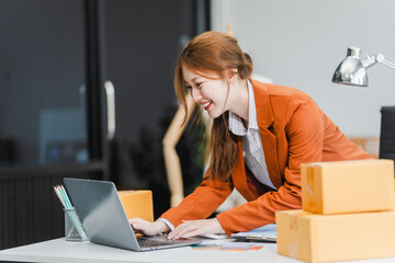 A young Asian businesswoman efficiently manages SMEs, utilizing her desk, tablet, laptop to handle...