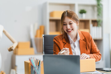 A young Asian businesswoman efficiently manages SMEs, utilizing her desk, tablet, laptop to handle...