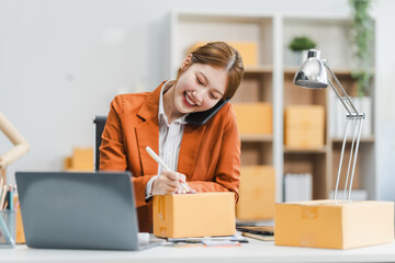 A young Asian businesswoman efficiently manages SMEs, utilizing her desk, tablet, laptop to handle...
