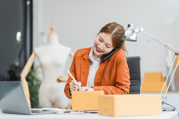 A young Asian businesswoman efficiently manages SMEs, utilizing her desk, tablet, laptop to handle...