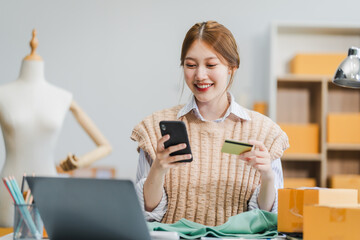 A young Asian businesswoman efficiently manages SMEs, utilizing her desk, tablet, laptop to handle...