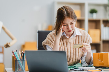 A young Asian businesswoman efficiently manages SMEs, utilizing her desk, tablet, laptop to handle...