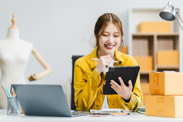 A young Asian businesswoman efficiently manages SMEs, utilizing her desk, tablet, laptop to handle...