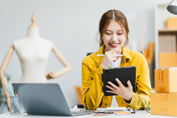 A young Asian businesswoman efficiently manages SMEs, utilizing her desk, tablet, laptop to handle...