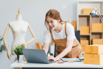 A young Asian businesswoman efficiently manages SMEs, utilizing her desk, tablet, laptop to handle...