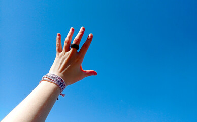 Friendship bracelets handmade of embroidery thread with knots. Female hand on blue sky background. Boho style hands jewelry accessories