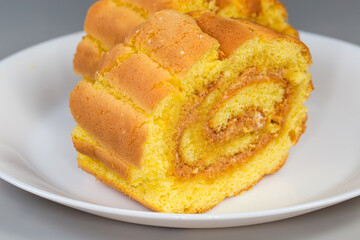Slices of lemon Swiss roll on dish on gray background