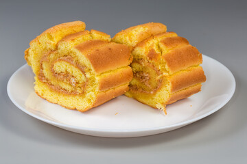 Slices of lemon Swiss roll on dish on gray background