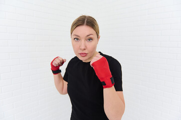 Confident waist up shot of a strong young woman punching forward a camera with boxing gloves,...