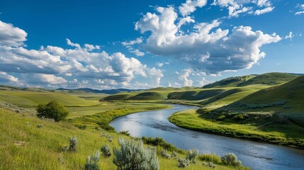 A river winds through a valley between green hills, under a blue sky with fluffy white clouds.