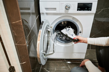 Dirty sport shoes need to be washed. Cropped photo of woman putting sneaker in washing machine.