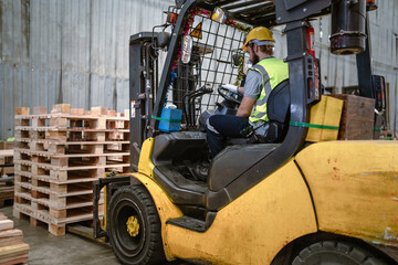 Warehouse worker wears safety helmet driving forklift truck in pallet factory. Skilled male...